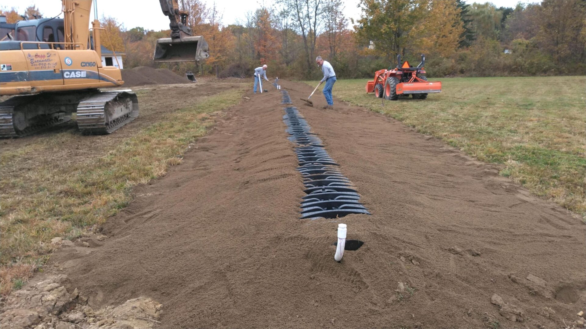 Two men raking sand over structure installed underground