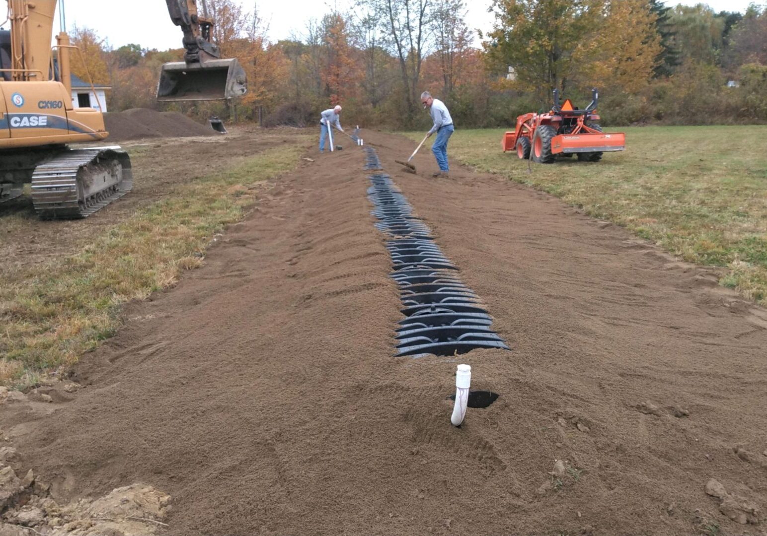 Two men raking sand over structure installed underground